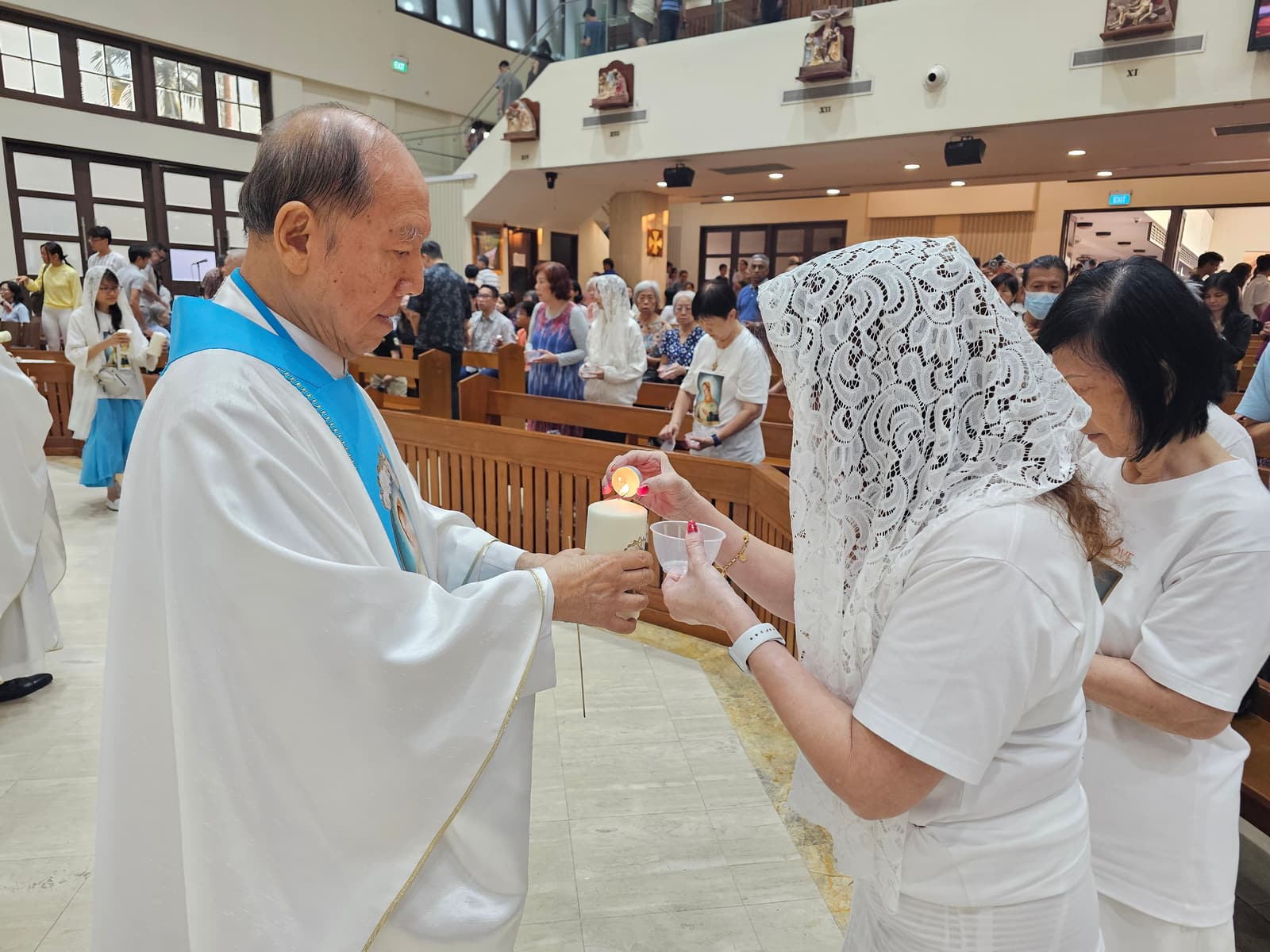 A priest in blue-and-white vestments passing the lit flame to a parishioner during the Blessing of Candles
