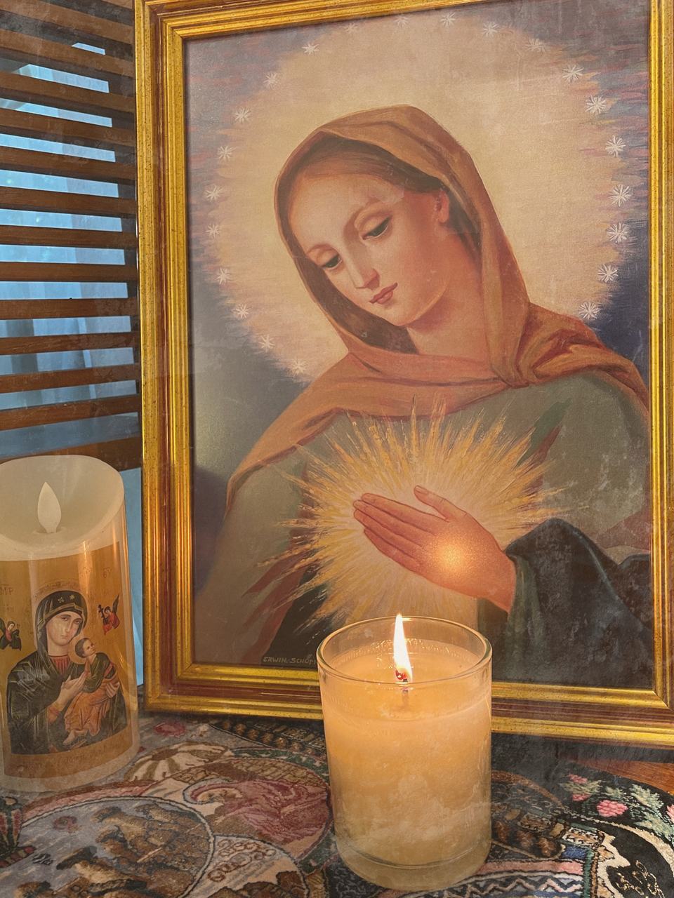 The framed Flame of Love image of Our Lady with a single lit votive candle burning before it