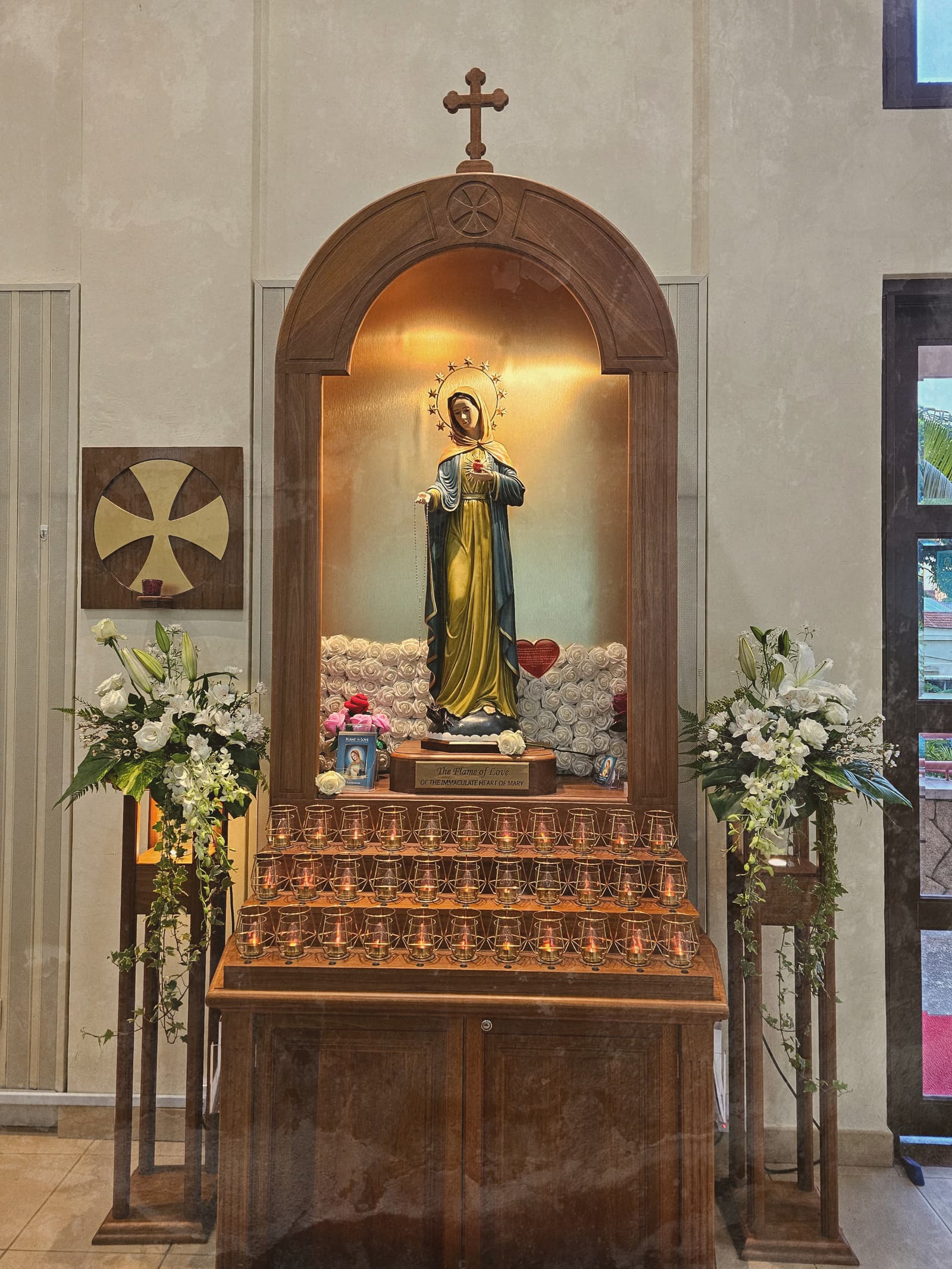 The Flame of Love shrine at the Church of the Immaculate Heart of Mary, the statue of Our Lady above banks of votive candles and white flowers